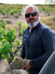 Photo of South African winemaker Adi Badenhorst in a vineyard holding a rock.