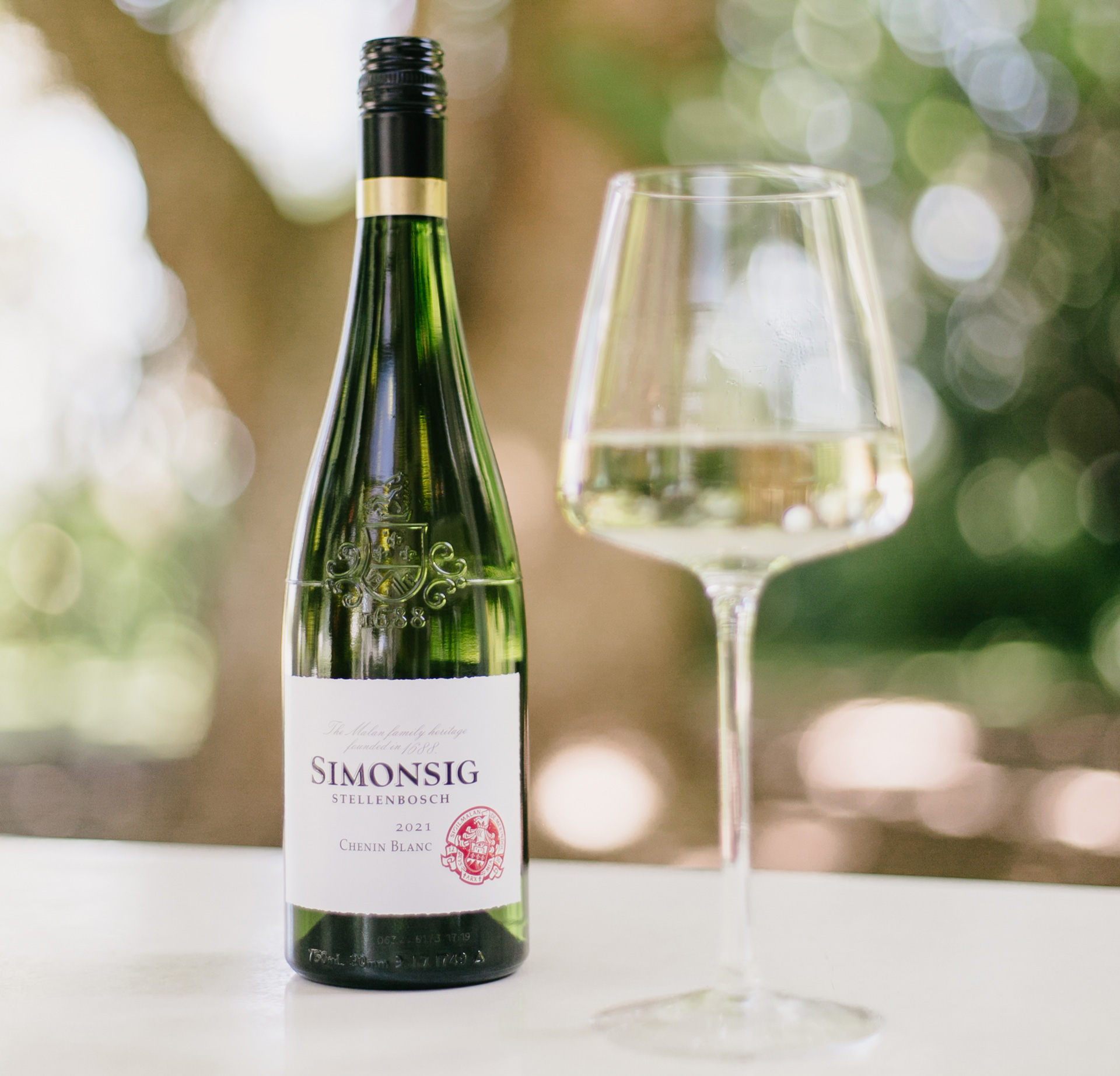 Bottle and poured glass of Simonsig Chenin Blanc, staged on a white table outdoors.