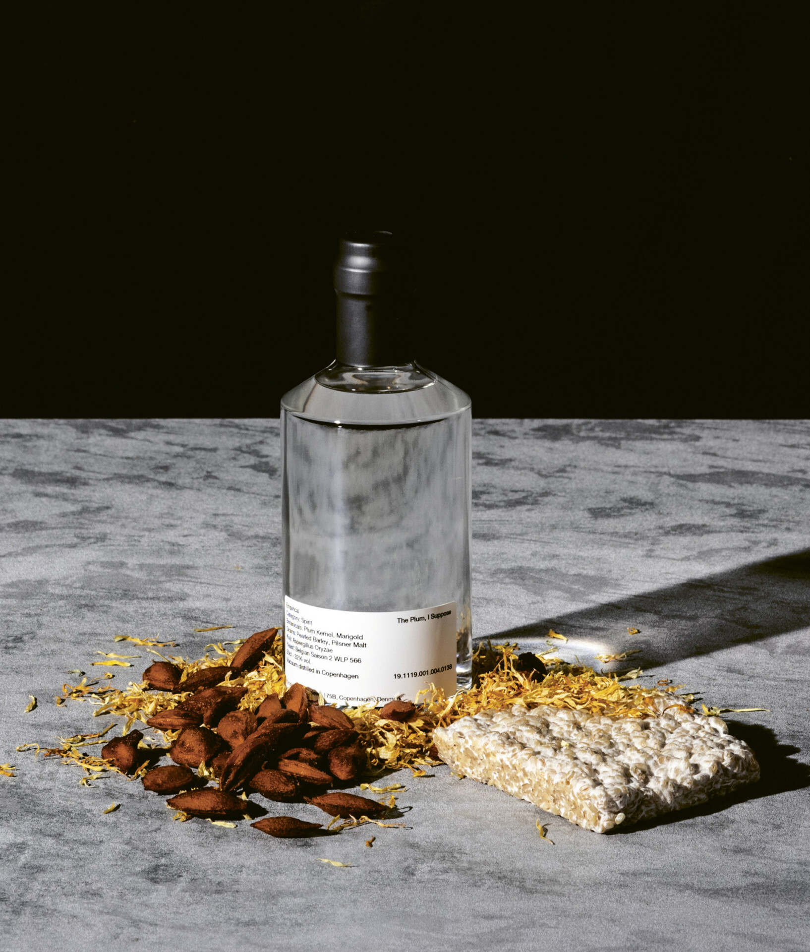A bottle of The Plum... I suppose from Empirical Spirits on a while marble table with a black background, with tasting notes like almonds and nougat next to the bottle.