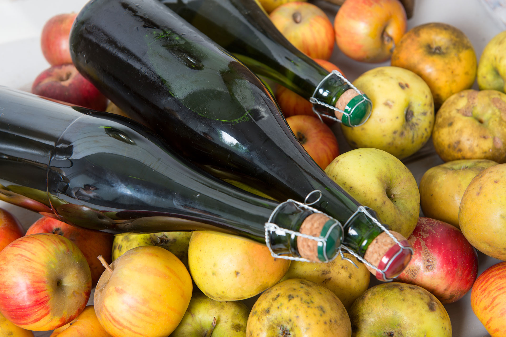 Cage and corked unlabeled bottles resting atop a spread of yellow, green and red apples.