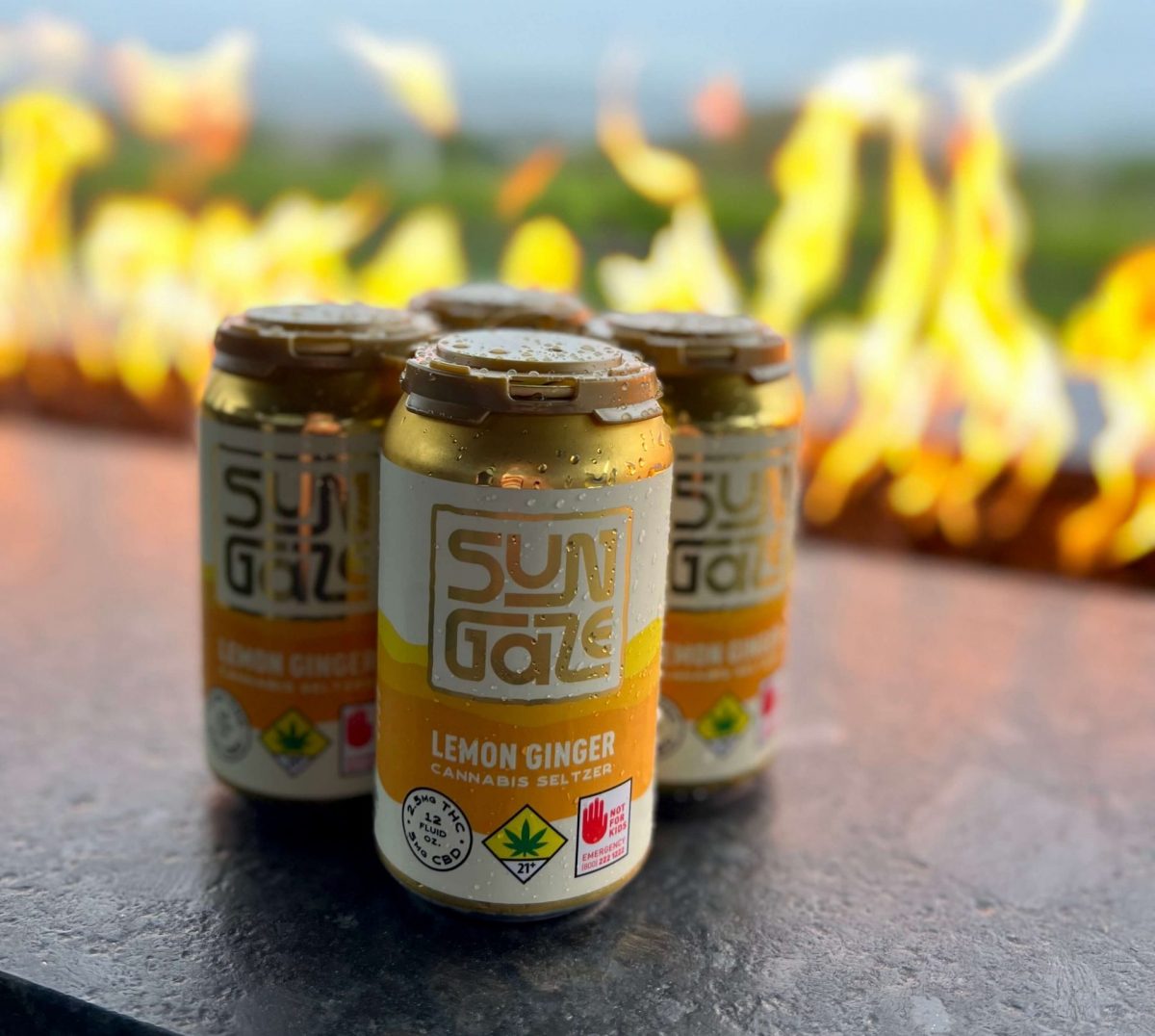 Cans of Sungaze on a countertop, with a firepit and landscape in the background.