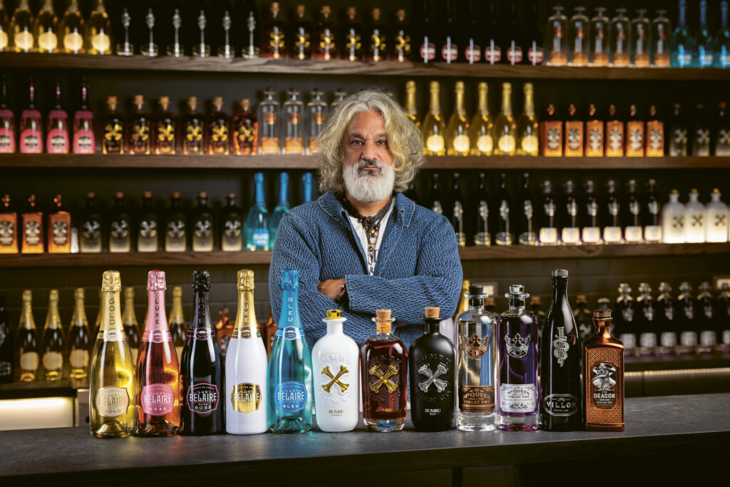 Photograph of Brett Berish standing behind a bar, arms folded, with a lineup of bottles from his Sovereign Brands portfolio in front of him.