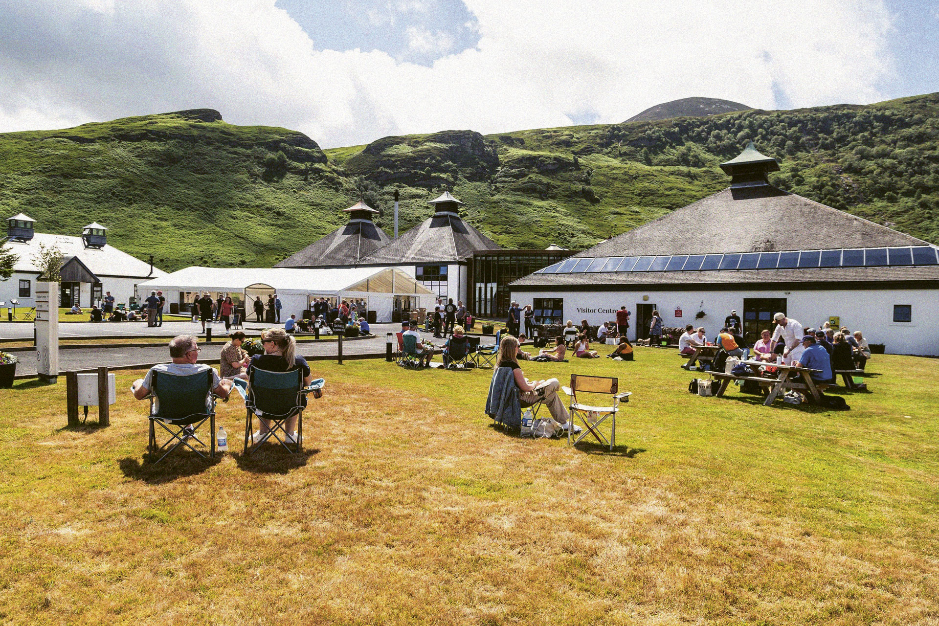 People gathered on a lawn outside with tents in the background for the Arran Whiskey Festival