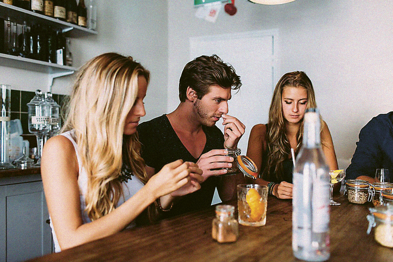 A man and two women smelling gin-making ingredients at a table with bottles in front of them at The Distillery in London.