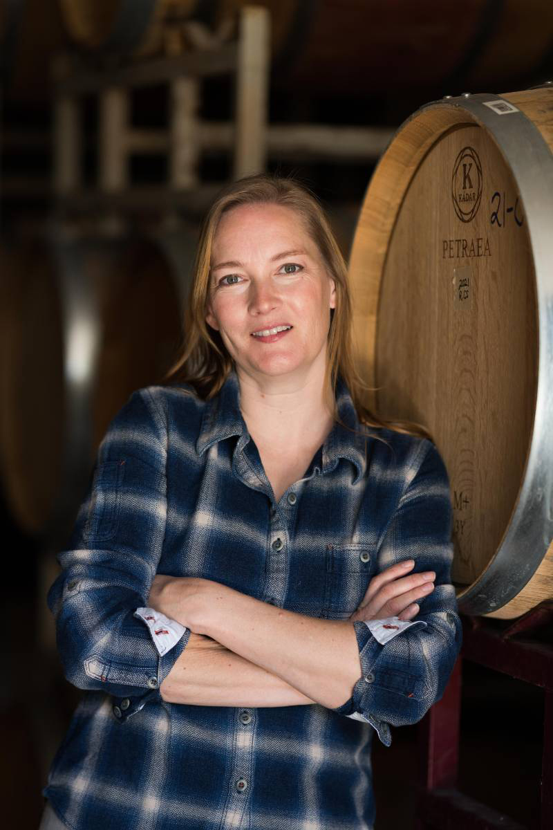 Photograph of Meredith Sarboraria, winemaker at Rodrigue Molyneaux Wine, standing cross arms in front of a wine barrel.