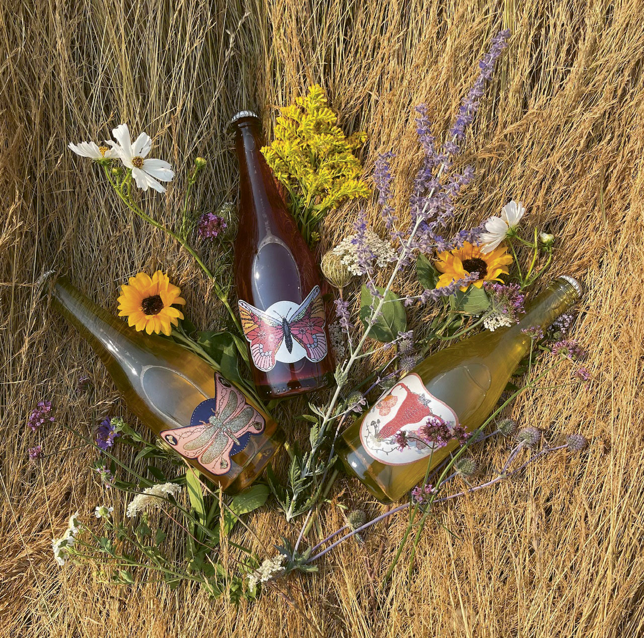 Three Art+Science bottles lying in dried grass surrounded by various herbs and flowers