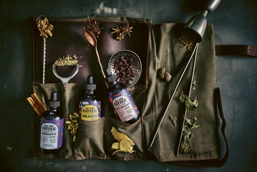 All the Bitter bottles on a green cloth alongside aromatic bittering ingredients like star anise, cinnamon and citrus peels.