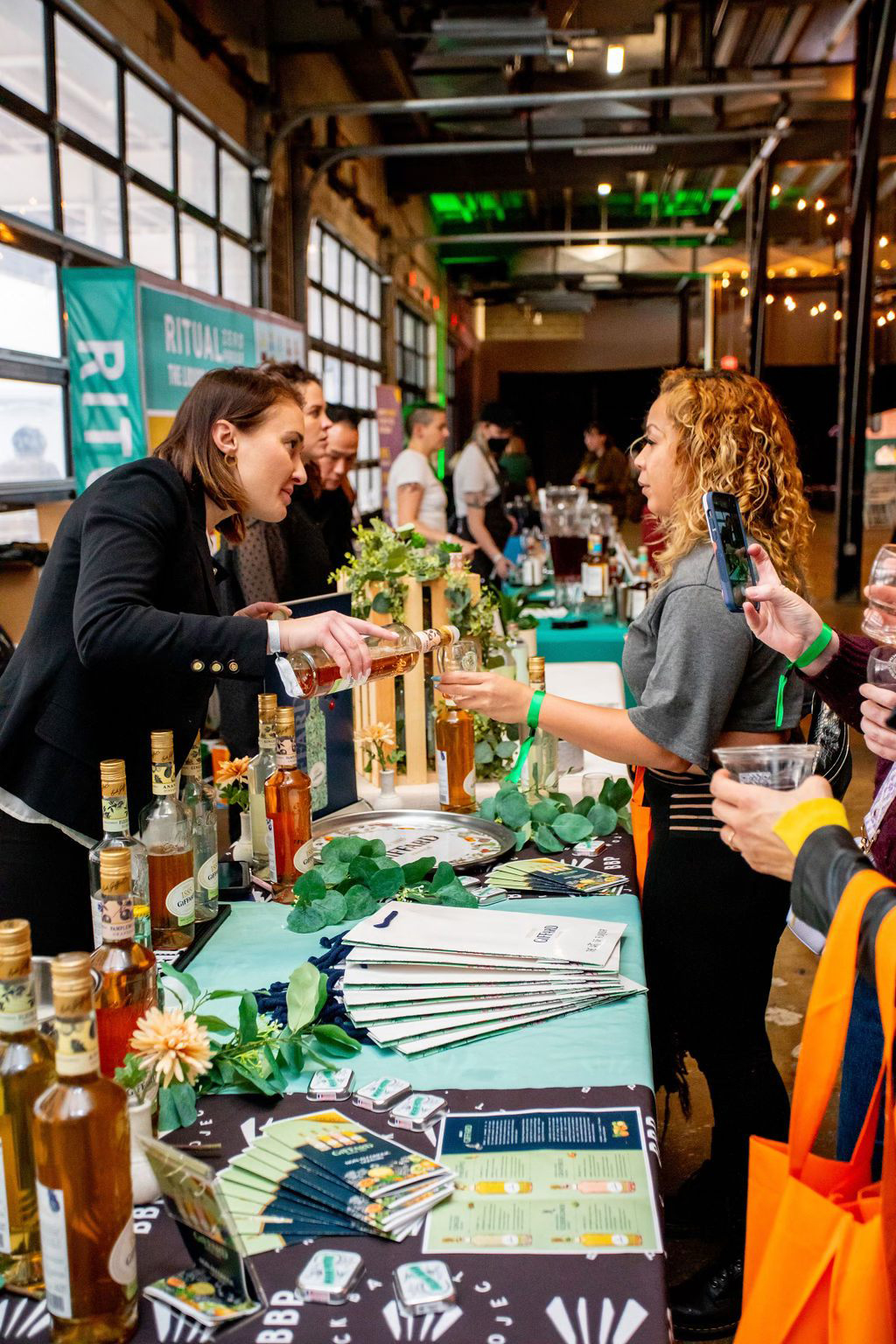 Tasting NA products at Mindful Drinking Fest 2024, showing a woman pouring a beverage sample for another woman at a festival table.