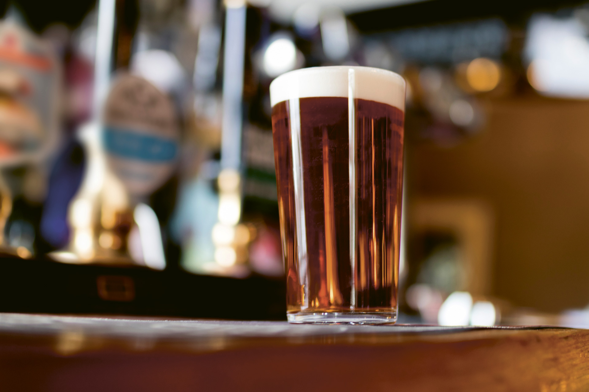 A cask ale pour on a bar with taps in the background.