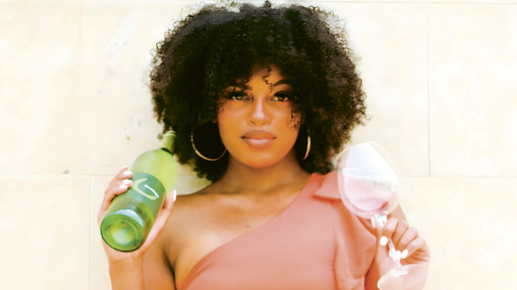 Head shot of Isis Daniel, holding a wine glass in one hand and wine bottle in the other.