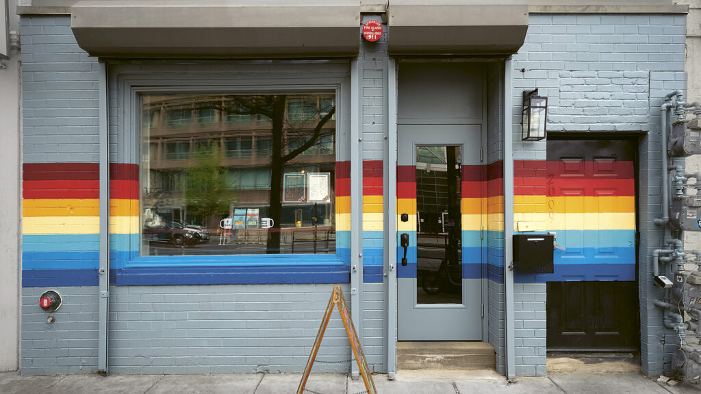 Spark-Hero Photograph of the front door and window of Spark Social House in Washington, DC, which features a rainbow banner painted horizontally across it.
