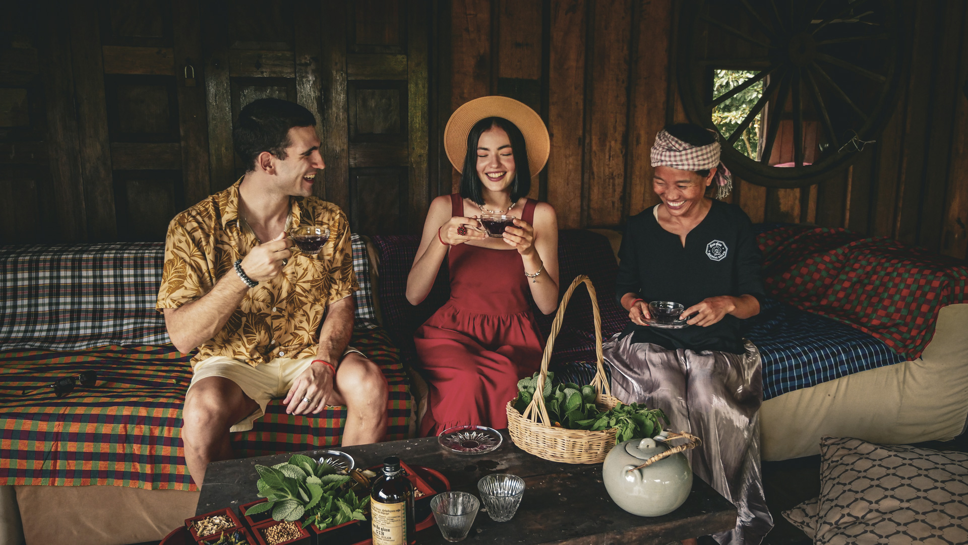 Herbal Kulen guest experience tasting, showing a distiller and two guests seated with glasses in hand and raw distillation ingredients on a table before them.