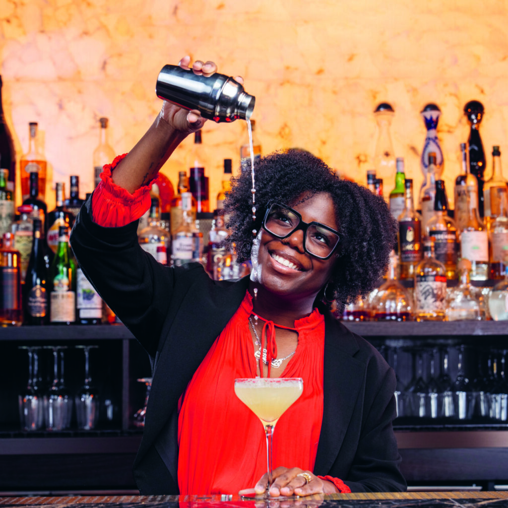 Photogrph of LP O'Brien, high pouring a drink with a smile behind a bar